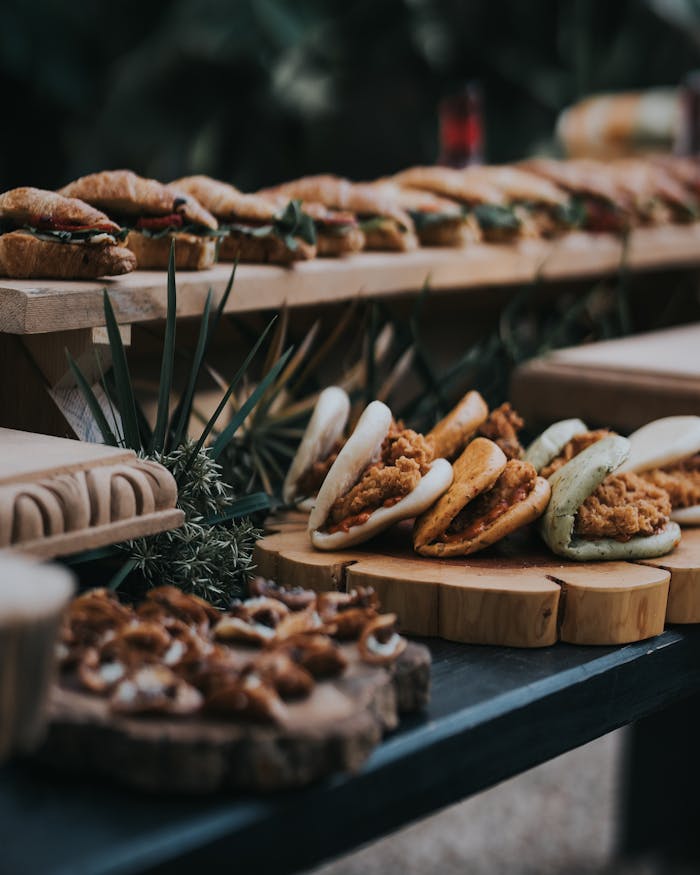 Services A variety of gourmet sandwiches displayed on rustic wooden platters at an outdoor event.